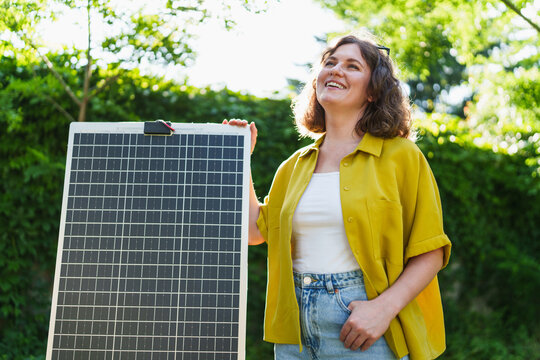 Woman standing in a green park holding a solar panel in the sunlight