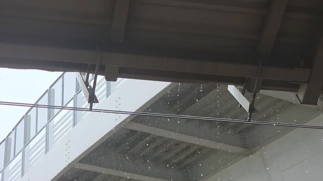 Rain falling under a bridge at a busy location during a cloudy day