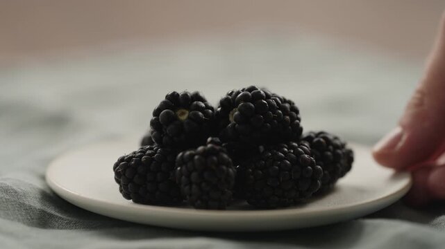 Slow motion man hand put fresh ripe blackberry on a white saucer
