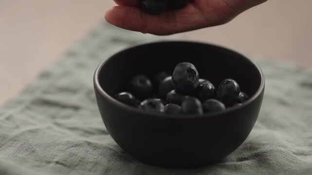 Slow motion man hand put blueberries to a ceramic bowl