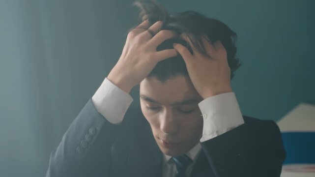 Asian businessman rubbing eyes showing fatigue, sit at desk with folders and plant, tie loosened, massaging temples and neck, eye strain and burnout relief, deep breath and composure, office pause
