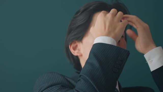 Young asian man in suit grooming hair and adjusting tie, editorial portrait series with teal backdrop, soft cinematic lighting, poised expression, preparing for presentation and leadership, model