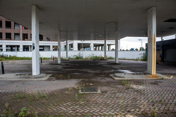 Disused petrol station forecourt with weathered canopy overgrown paving and rusting support column © Philip