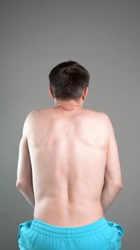 Unrecognizable man performs exercises for muscles of upper back, arms and shoulder joint. Posture correction and physical therapy on gray background