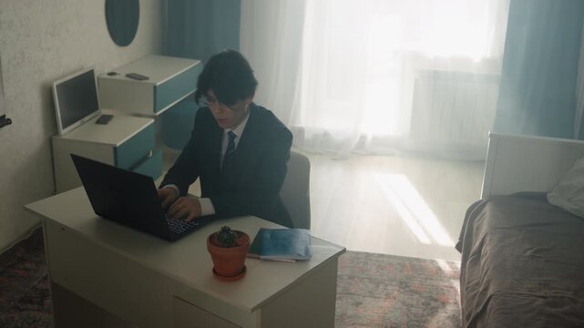Asian professional working late in apartment, sunlit living area with low table, laptop, face mask and potted plant on table alternates between freelancer, student, and startup founder roles