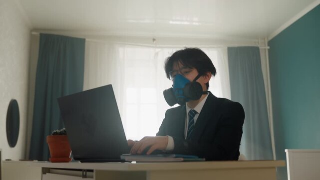 Young professional in suit wearing respirator at laptop, typing in quiet home office with potted plant, soft window light and teal walls, corporate analyst reviewing reports and joining virtual