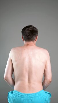Unrecognizable man performs exercises for muscles of upper back, arms and shoulder joint. Posture correction and physical therapy on gray background