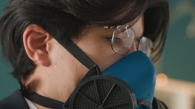 Closeup asian man wearing respirator and safety glasses inspecting mask seal, technician adjusting filter and strap in clinical workspace, soft bokeh background, warm lighting, meticulous and cautious