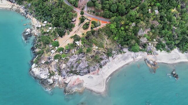 Aerial drone shot reveals a tropical beach framed by granite formations, turquoise seas, dense greenery, sandy cove, coastal roads, and natural appeal