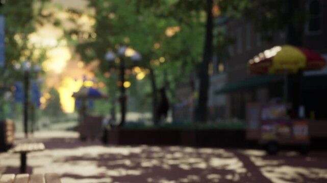 People stroll through a city park during sunset. Benches line the path while food stalls are set up nearby. Trees provide shade as sunlight filters through the leaves.
