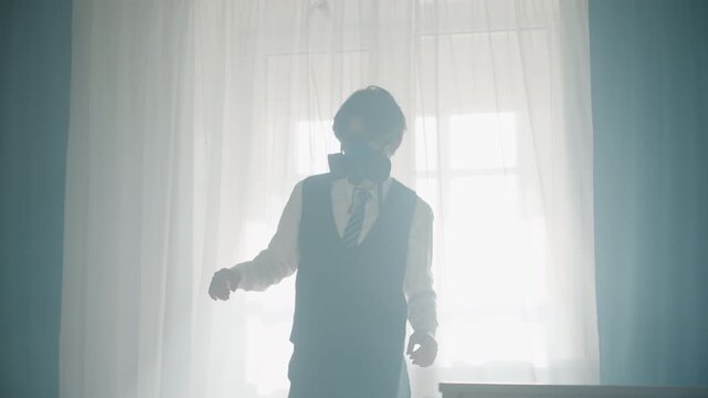 Young man in tie walking along window, soft haze and backlight, slow pacing and introspective posture, respirator worn, cinematic solitude and melancholic atmosphere captured in full silhouette