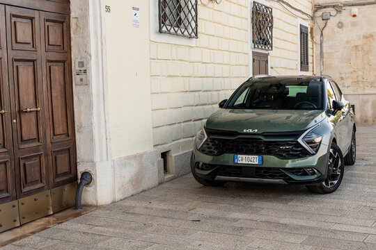 Bari, Italy - June 31, 2026: Kia Sportage SUV in dark green parked near historic building entrance on stone pavement in old town district