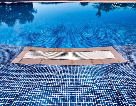 overhead close up of a swimming pool drain surrounded by blue mosaic tiles and clear water highlighting symmetry texture and modern minimalist design