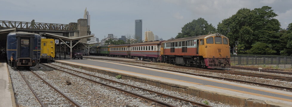 View of multiple train carriages and a classic orange diesel locomotive resting on open rail tracks at Hua Lamphong train station in Thai capital Bangkok