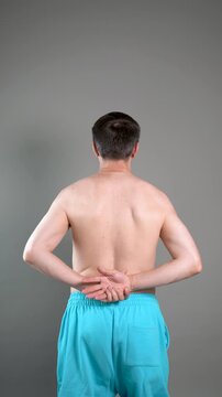 Unrecognizable man performs exercises for muscles of upper back, arms and shoulder joint. Posture correction and physical therapy on gray background