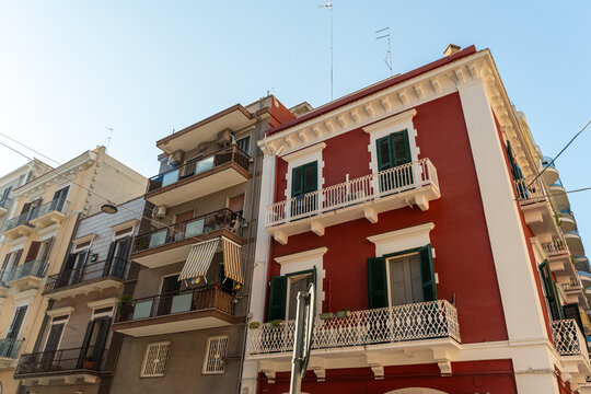Colorful apartment buildings in Bari, Italy with red facade, green shutters and ornate white balconies on sunny day, concept of Mediterranean urban architecture