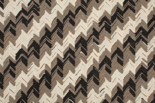 A repeating chevron pattern featuring zigzag lines in shades of black, gray, and beige with a hand-drawn textured appearance on a light base