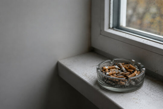Ashtray full of cigarette butts on windowsill. Space for text.