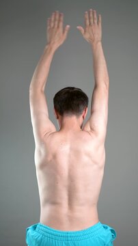 Unrecognizable man performs exercises for muscles of upper back, arms and shoulder joint. Posture correction and physical therapy on gray background