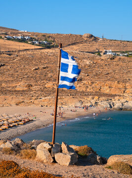The Greek flag on the rocks against the backdrop of the Aegean Sea on Mykonos Island in Greece