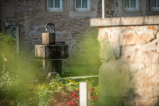 Selektiver Fokus wegen Wassermangel leergelaufener Brunnen mit Steinquadern aus Sandstein am Kirchplatz der evangelischen Kirche St. Martin in Neckartenzlingen