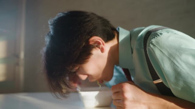 Asian student savoring steaming bowl, leaning in for slurp, warm broth and noodles, sunlight and kitchen lamp highlights, smile and small fist pump, comfort and satisfaction after tense moment