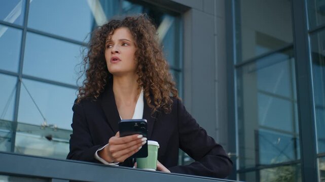 Caucasian irritated business woman checking time with mobile phone waiting meeting in city near office building stressed businesswoman female girl agent wait with coffee and smartphone outside company