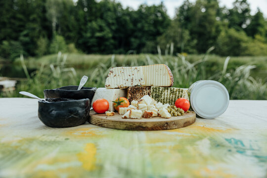 Rustic assortment of fresh and seasoned goat cheeses with tomatoes, preserves, creamy spread and marinated cheese jars, arranged outdoors for a local food tasting