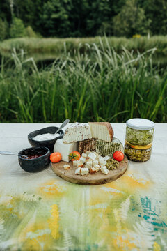 Rustic assortment of fresh and seasoned goat cheeses with tomatoes, preserves, creamy spread and marinated cheese jars, arranged outdoors for a local food tasting