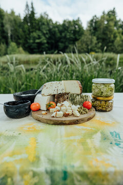 Rustic assortment of fresh and seasoned goat cheeses with tomatoes, preserves, creamy spread and marinated cheese jars, arranged outdoors for a local food tasting