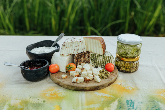 Rustic assortment of fresh and seasoned goat cheeses with tomatoes, preserves, creamy spread and marinated cheese jars, arranged outdoors for a local food tasting