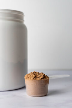 Protein powder in a scoop with container on a light surface 