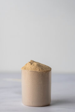 Protein powder in a scoop with container on a light surface 