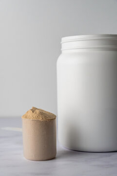 Protein powder in a scoop with container on a light surface 