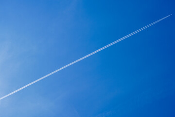 Airplane with two parallel contrails flying across clear deep blue sky, diagonal composition, vast empty sky background © YongQin