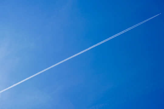 Airplane with two parallel contrails flying across clear deep blue sky, diagonal composition, vast empty sky background