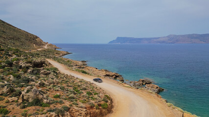 Aerial view of black car driving along coastal dirt road near turquoise sea water during summer road trip in Crete Greece © moryachka