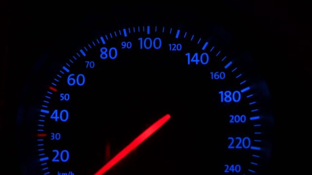 Illuminated car speedometer dashboard at night. Modern car instrument cluster with glowing blue numbers and red needle.