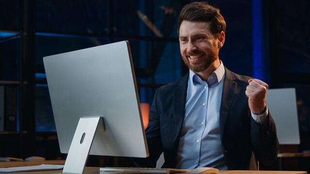 Happy Caucasian middle-aged business man winning typing computer at night dark office mature businessman smiling win with online success male entrepreneur rejoice victory finish job achieve at evening