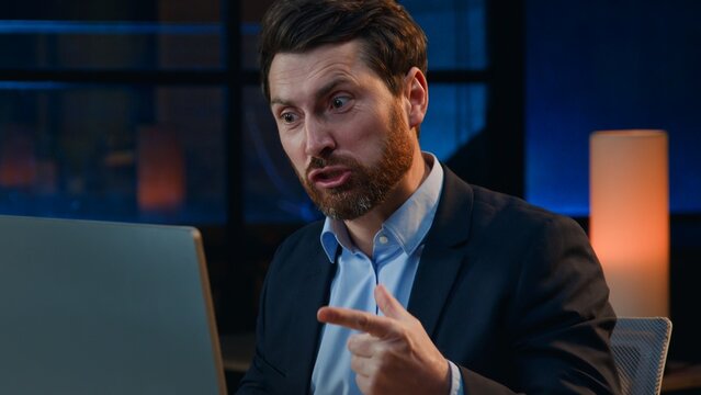 Stressed angry irritated Caucasian middle-aged business man yelling in computer at night dark office annoyed mature businessman male employer yell to laptop deadline overworked problem rage at evening