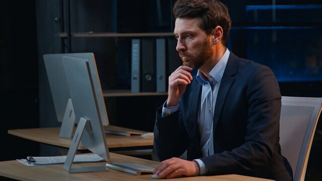 Serious hesitate busy Caucasian business man working with computer think at night office middle-aged businessman male manager work with online corporate project software thinking overtime at evening