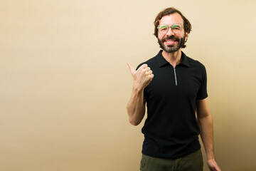 Fototapeta premium Happy bearded man in glasses giving thumbs up and pointing approvingly to a commercial empty space