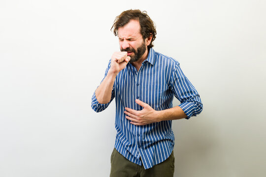 Man suffering from a cough, holding his hand to his mouth and a hand on his stomach due to illness symptoms