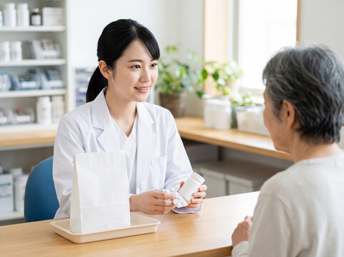 カウンター越しに薬瓶と錠剤を提示して説明する白い服の女性