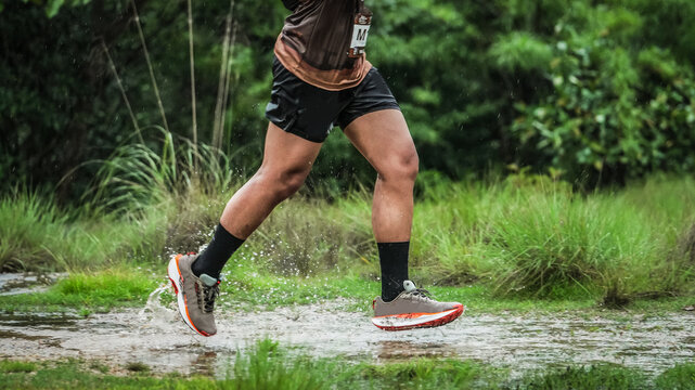 Trail runner splashing through water on a muddy outdoor path during an endurance race