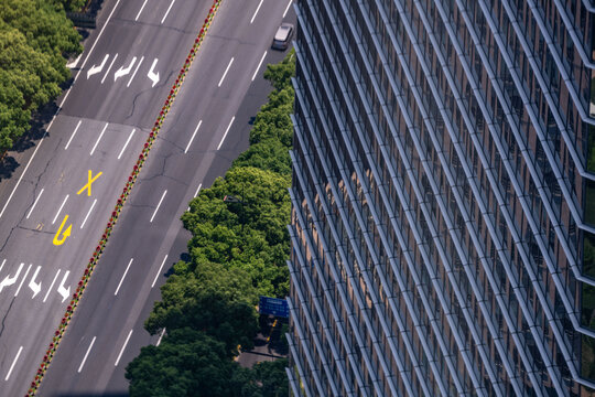 Aerial study of a lightly trafficked arterial route through a dense business district, kerbside planting running unbroken along the carriageway edge, the painted rules of a crowded district.