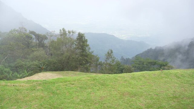 Viewpoint of Phu Thap Boek on high hill mountain and green grass lawn garden with nature fog mist and clouds sky for white misty and foggy view in rainy season by motion pan at Phetchabun in Thailand