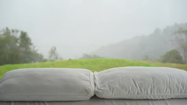 View of Phu Thap Boek garden home resort in bedroom with white dual pillow on double bed and rain dew on glass wall on high hill mountain in green lawn garden with fog mist and clouds sky in Thailand
