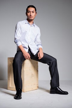 Asian sexy man wearing a white shirt and suit pants against a gray background