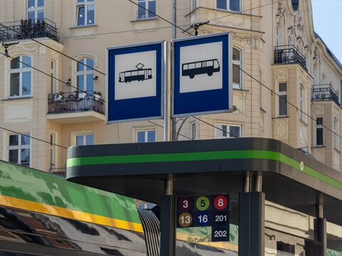 A public transport stop sign featuring symbols for trams and buses with route numbers standing against a classic European city building for urban commuting and city mobility travel